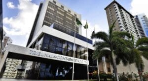 Sede do Tribunal de Contas do Estado do Rio Grande do Norte (TCE-RN), em Natal, com fachada moderna e bandeiras, tema do curso Discursiva na Prática para a prova discursiva do concurso.